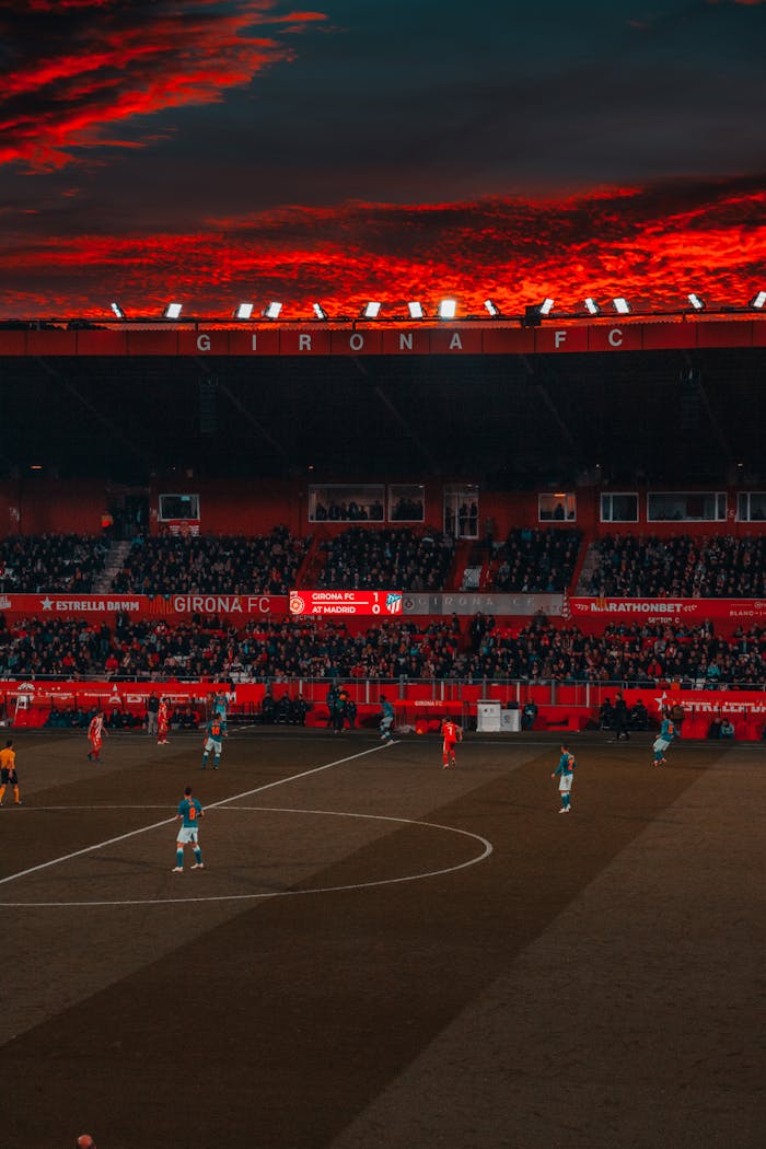 Dramatic evening soccer game at Girona FC stadium with vibrant red sky and intense play.