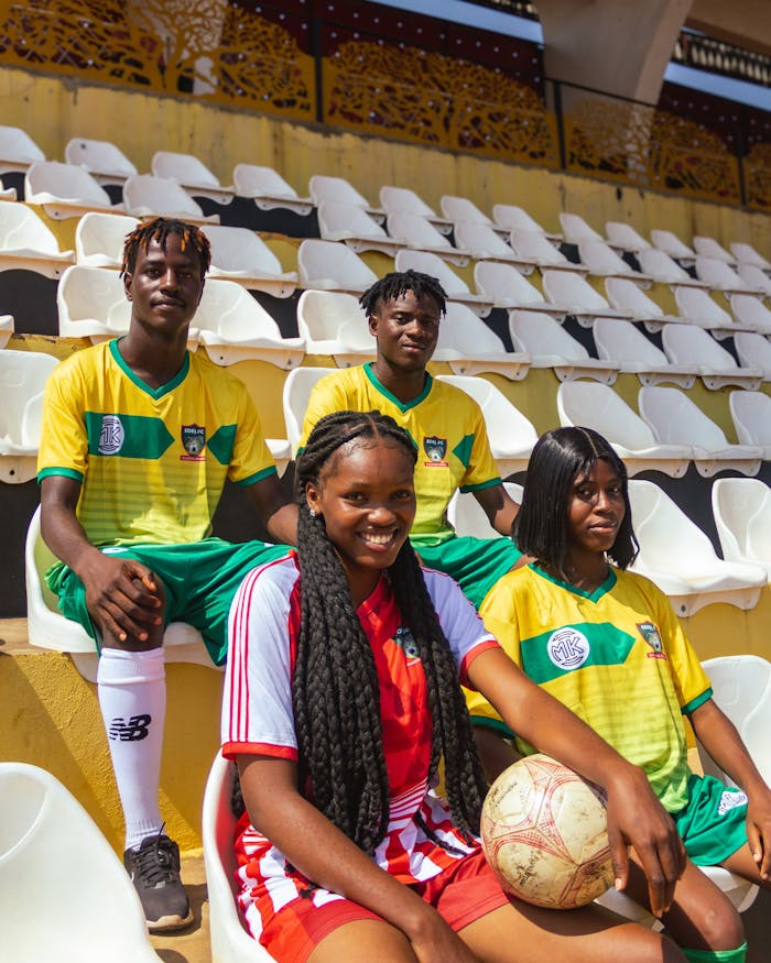 Four young soccer players pose in team uniforms inside an empty stadium.